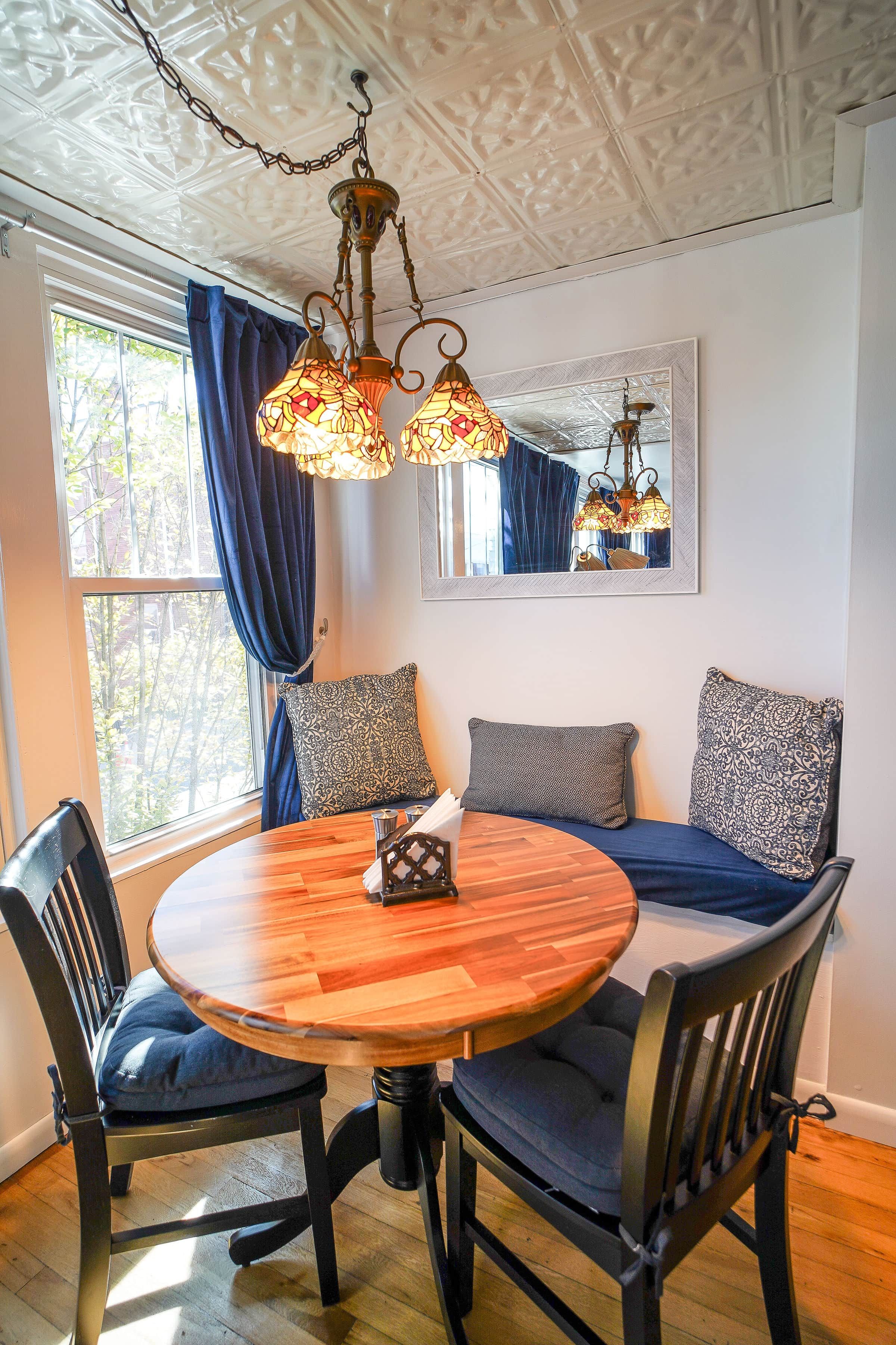 A dining area with a round wooden table, four chairs, and a bench with patterned cushions.
