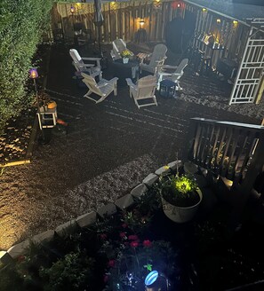 An outdoor seating area with Adirondack chairs and a table, surrounded by a wooden fence and potted plants.