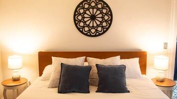 A hotel room with a neatly made bed, two bedside lamps, and a decorative wall piece above the bed.