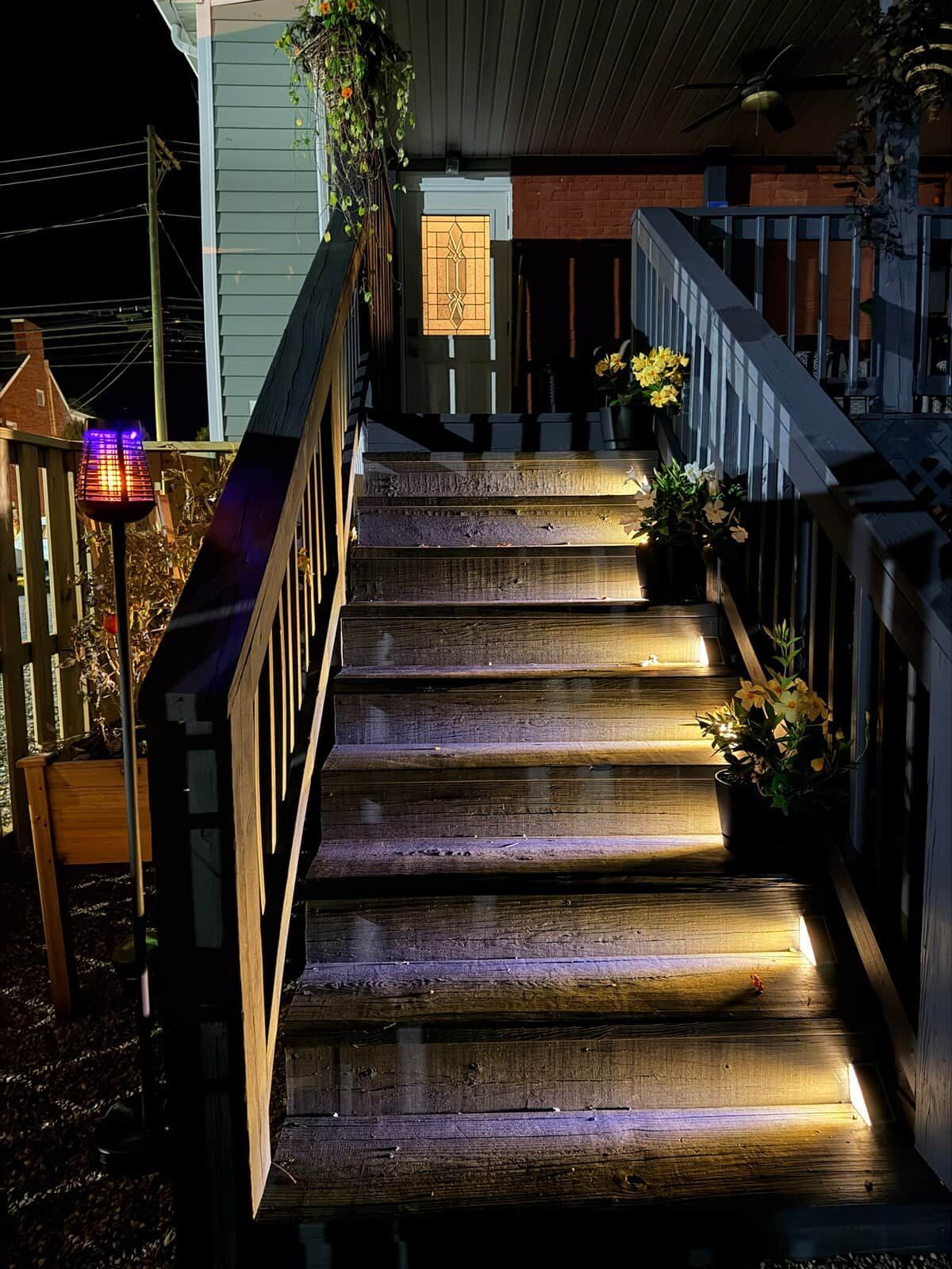 A wooden staircase with a railing, leading to a door with a geometric glass design.