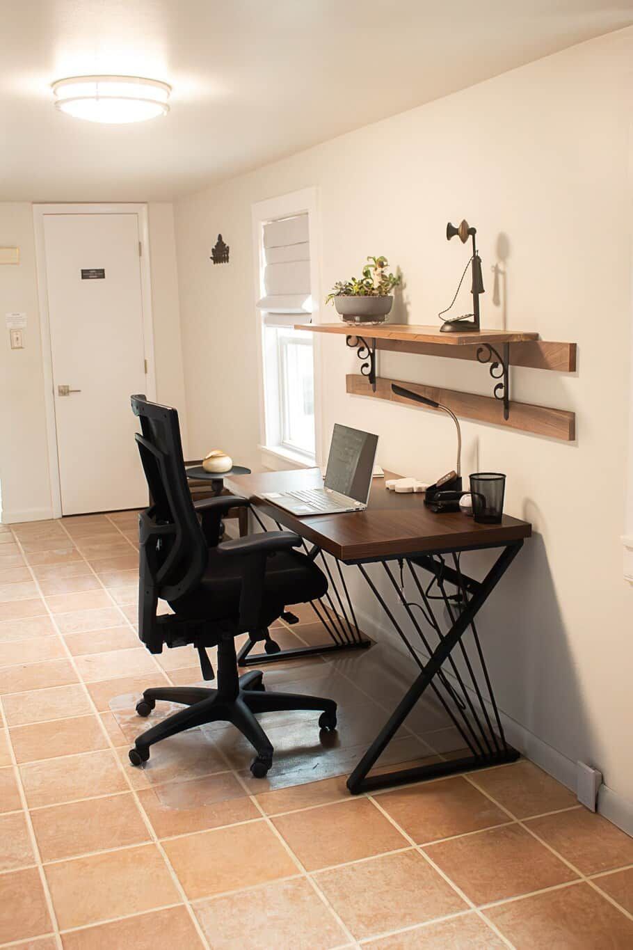 A home office with a desk, chair, laptop, and shelves with decorative items.
