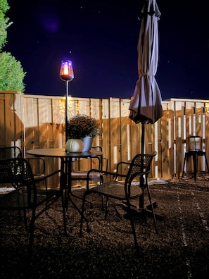 Un patio al aire libre con una mesa redonda, cuatro sillas, una planta en maceta y un parasol colgante.