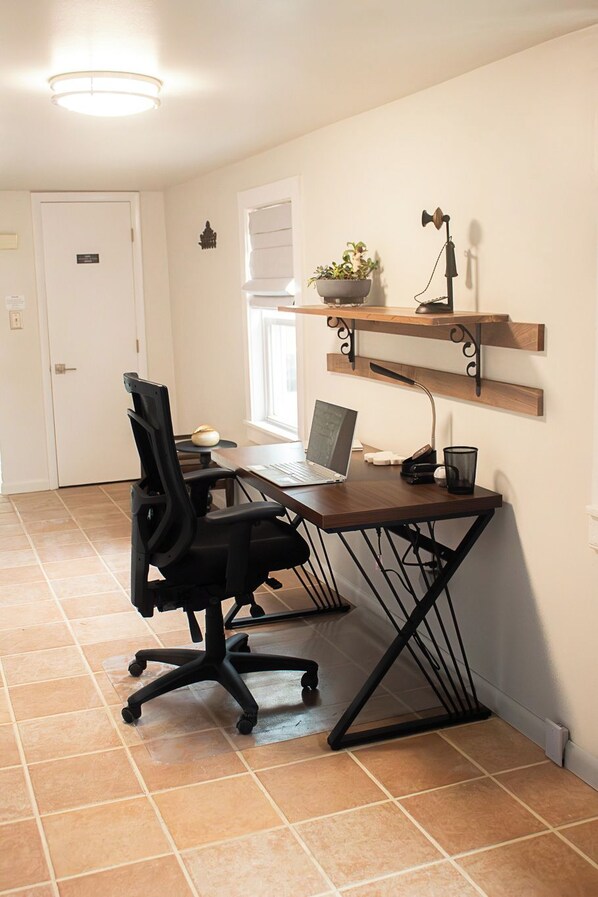 A home office with a desk, chair, laptop, and shelves with decorative items.