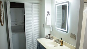 Un baño con lavamanos blanco, un espejo y zona de ducha.