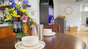 Una mesa de comedor con platos y tazones blancos, un florero de cristal con flores y una botella de vino.