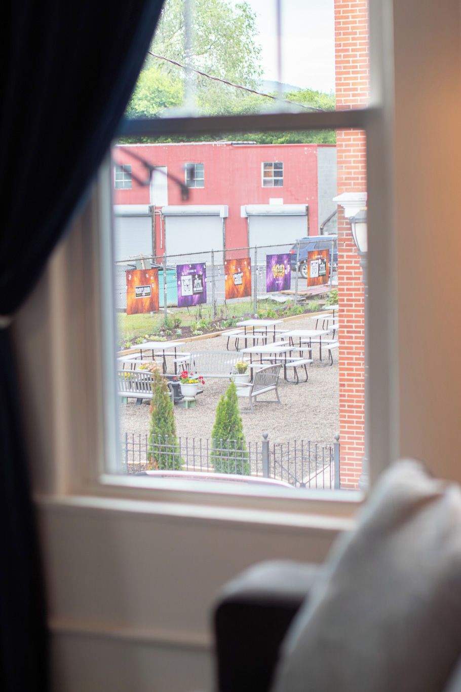 A window view of an outdoor area with a brick building, tables, and chairs.