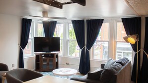 Una sala de estar con televisor de pantalla plana, un sofá, una mesa de centro y una lámpara.