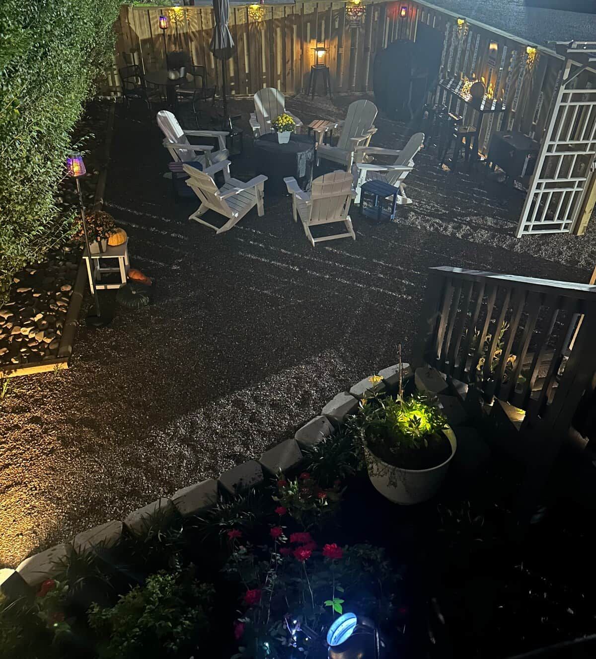 An outdoor seating area with chairs and tables, surrounded by a wooden fence and decorative lighting.