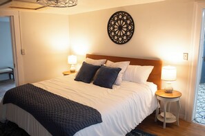 Ein ordentlich bezogenes Bett mit weißer Daunendecke und dunklen Kissen, zwei Nachttischlampen und einem dekorativen Wandbild.
