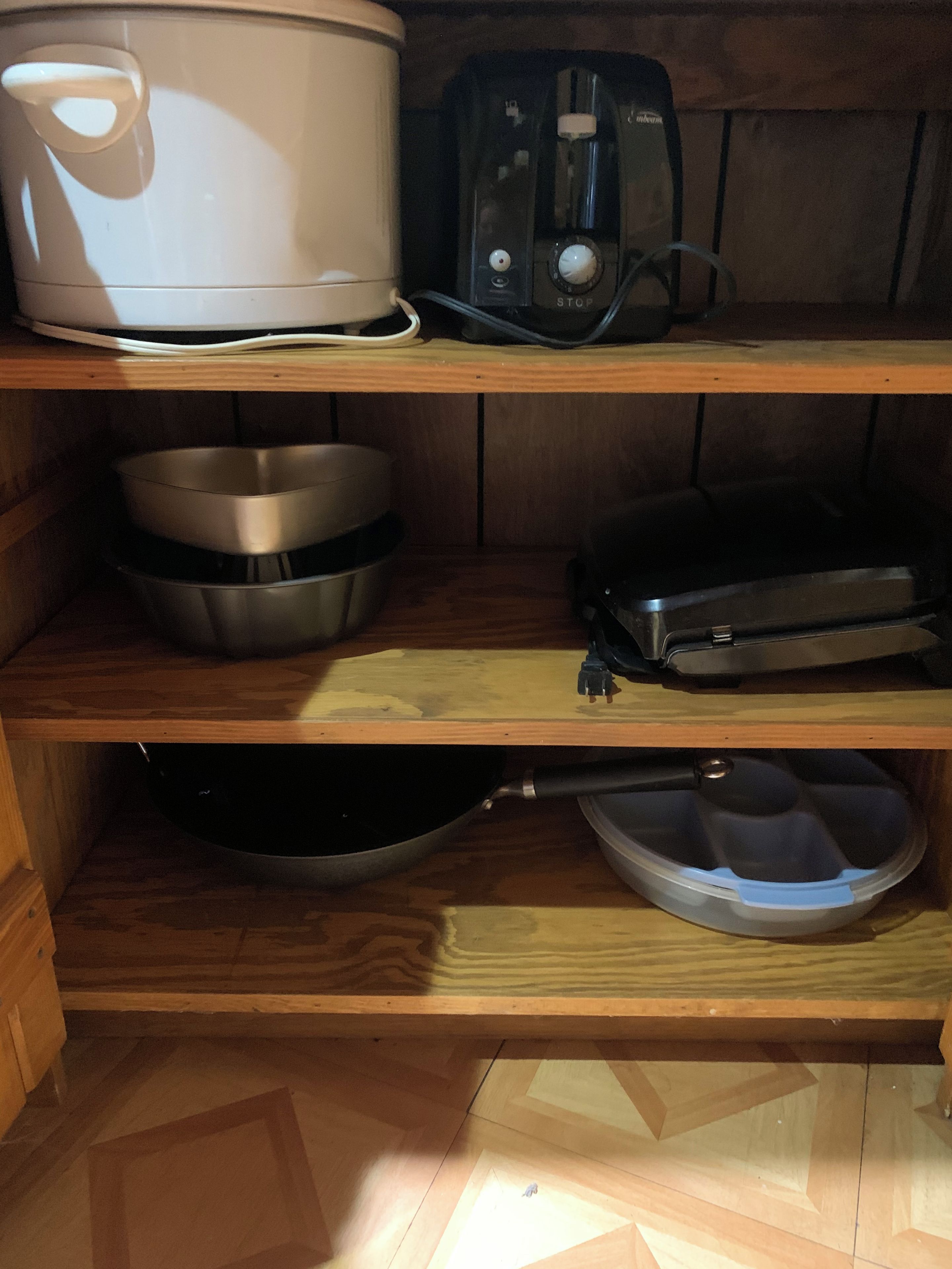Una cocina con una olla de cocción lenta, un tostador, boles de acero inoxidable, una sartén y un recipiente de plástico sobre estantes de madera.