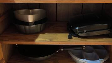 Una cocina con una olla de cocción lenta, un tostador, boles de acero inoxidable, una sartén y un recipiente de plástico sobre estantes de madera.