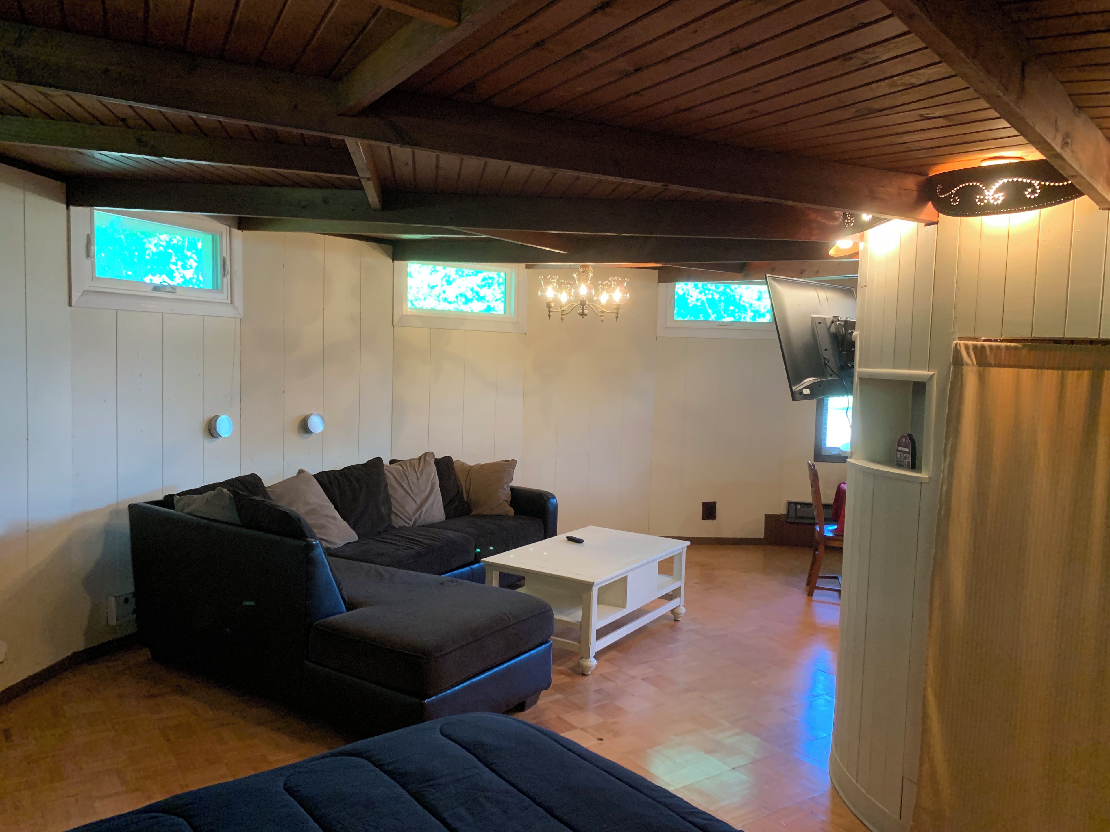 A cozy living room with a sectional sofa, a white coffee table, and a television mounted on the wall.