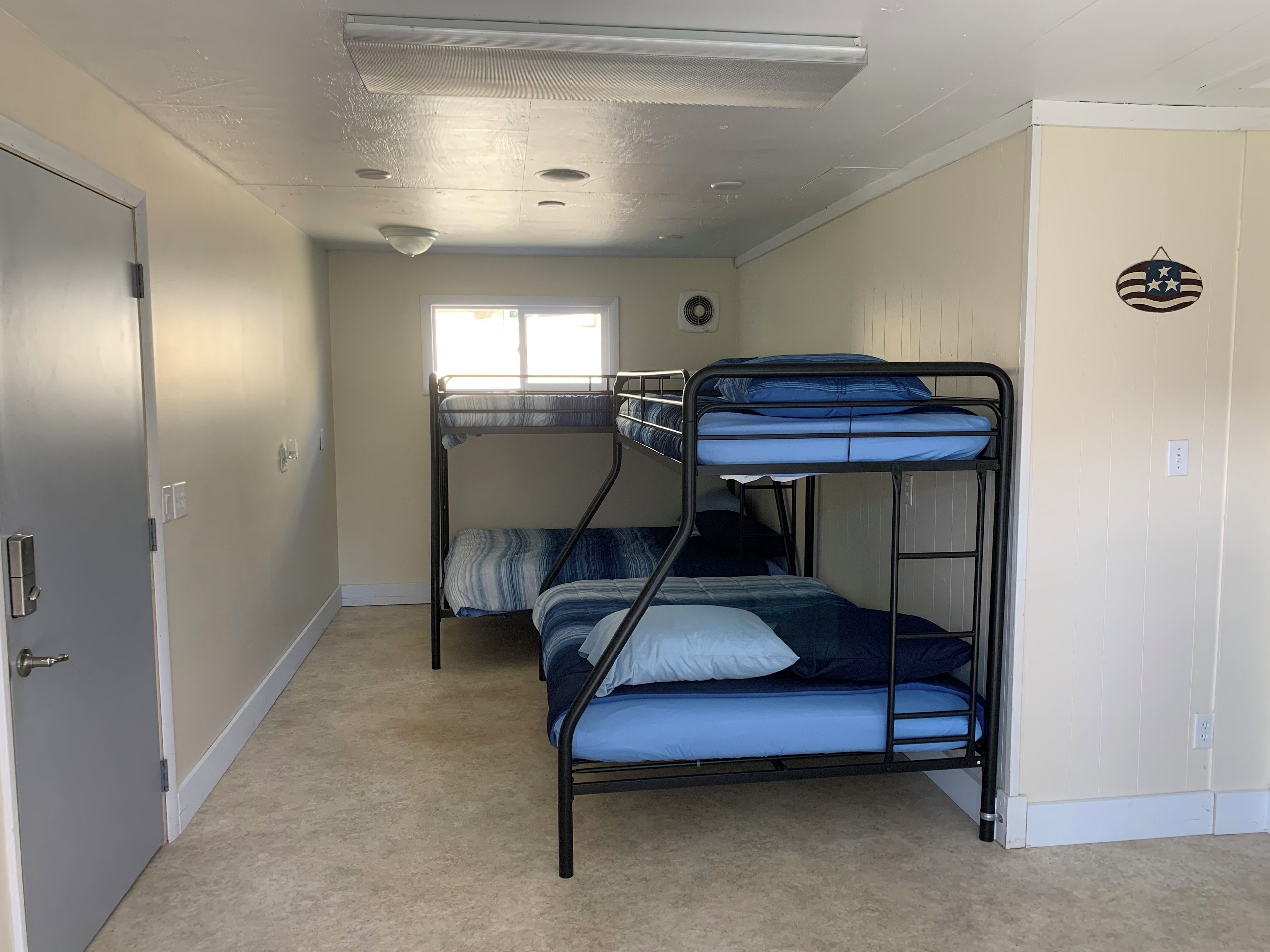 A room with bunk beds, a window, a door, and a wall-mounted light fixture.