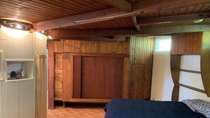 Ein Schlafzimmer mit Holzboden, einem Bett mit blauer Bettdecke und einem Schrank mit Spiegel.