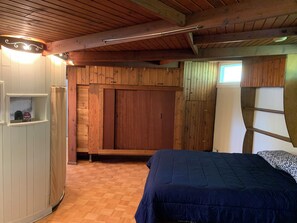 A bedroom with a wooden ceiling, a bed with a blue bedspread, and a wardrobe with a mirror. - Cozy 2-bedroom converted grain bin, check listing for bedroom details (Covington)