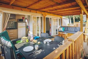 Ein überdachter Essbereich im Freien mit einem Tisch für zwei Personen, Stühlen, einer Couch und einer Holzterrasse.