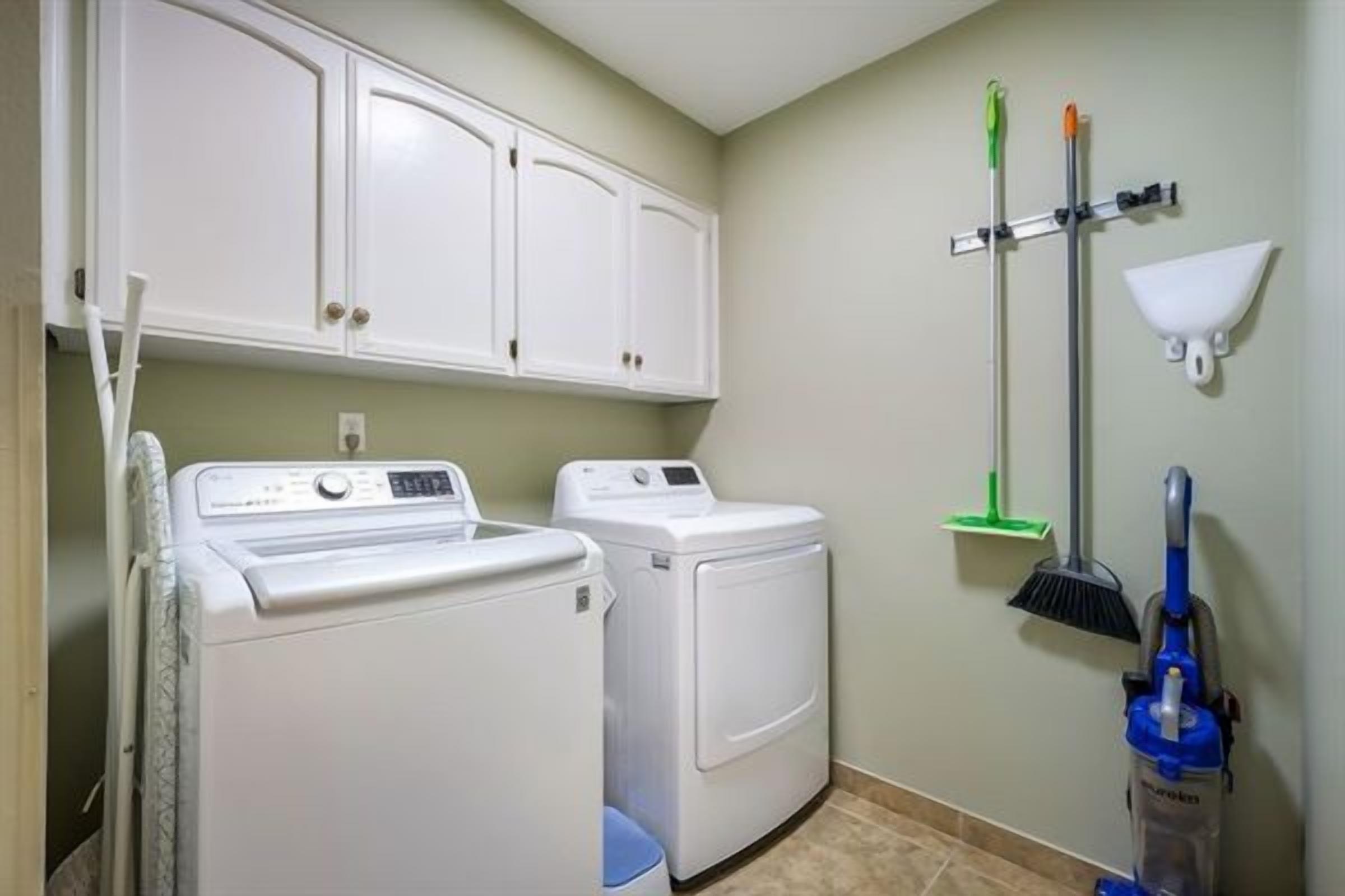 A laundry room with a washing machine, dryer, cabinets, and cleaning tools.