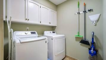 A laundry room with a washing machine, dryer, cabinets, and cleaning tools.