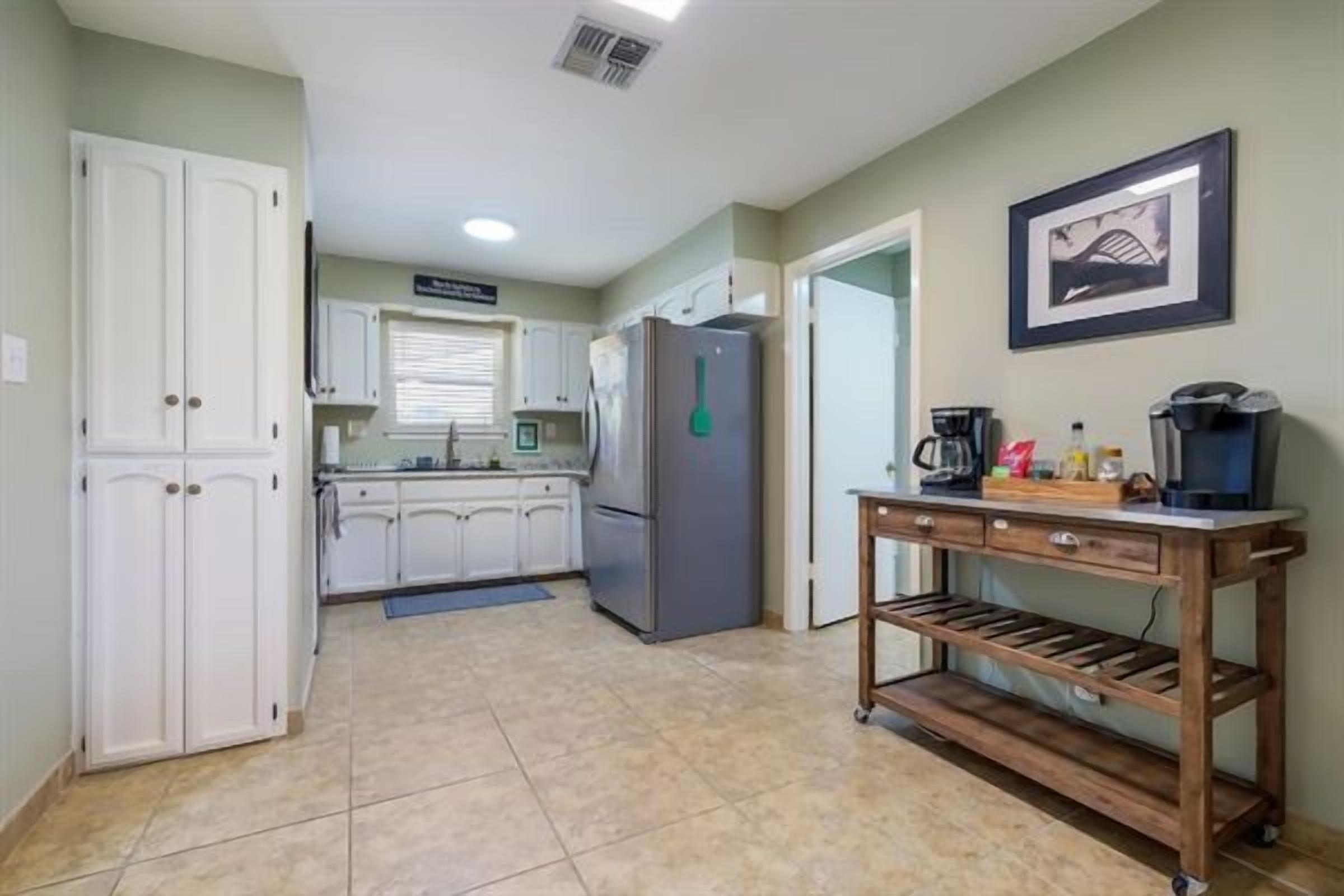A kitchen with white cabinets, a refrigerator, a coffee maker, and a shelf unit.
