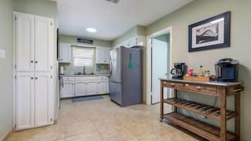 A kitchen with white cabinets, a refrigerator, a coffee maker, and a shelf unit.