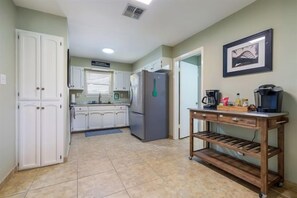 A kitchen with white cabinets, a refrigerator, a coffee maker, and a shelf unit. - Lake Retreat / 2 Private Sides / King Beds / Kayak (Seguin)