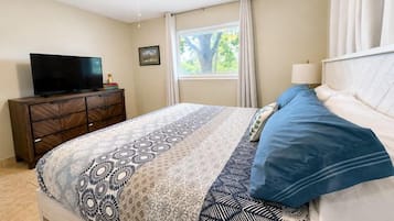 A bedroom with a bed, a television on a dresser, a window with curtains, and a ceiling fan.