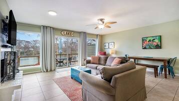 A living room with a sofa, a TV, a ceiling fan, and a dining area with a table and chairs.