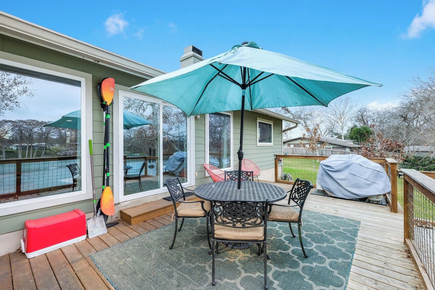 Een overdekt terras met een tafel, stoelen en een grote parasol, en een kajak die tegen de muur staat.