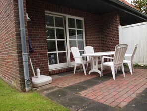 Eine Terrasse mit einer Ziegelwand, einem weißen Tisch und Stühlen sowie einem weißen Zaun.