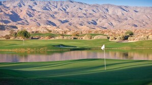 Campo de golf con una bandera, un estanque y montañas al fondo.