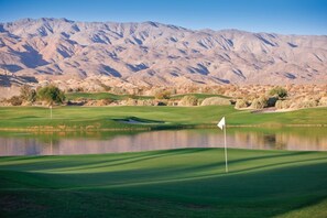 A golf course with a flag, a pond, and mountains in the background. - WM BLOCK Indio Studio (Indio)