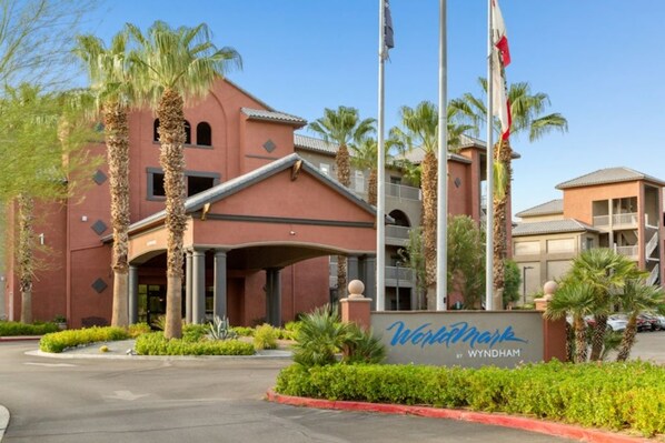 A hotel entrance with a red facade, palm trees, and a sign that reads 'Wyndham by Wyndham.' - WM BLOCK Indio Studio (Indio)