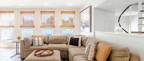 A modern living room with a sectional sofa, a glass coffee table, and a large window with blinds.