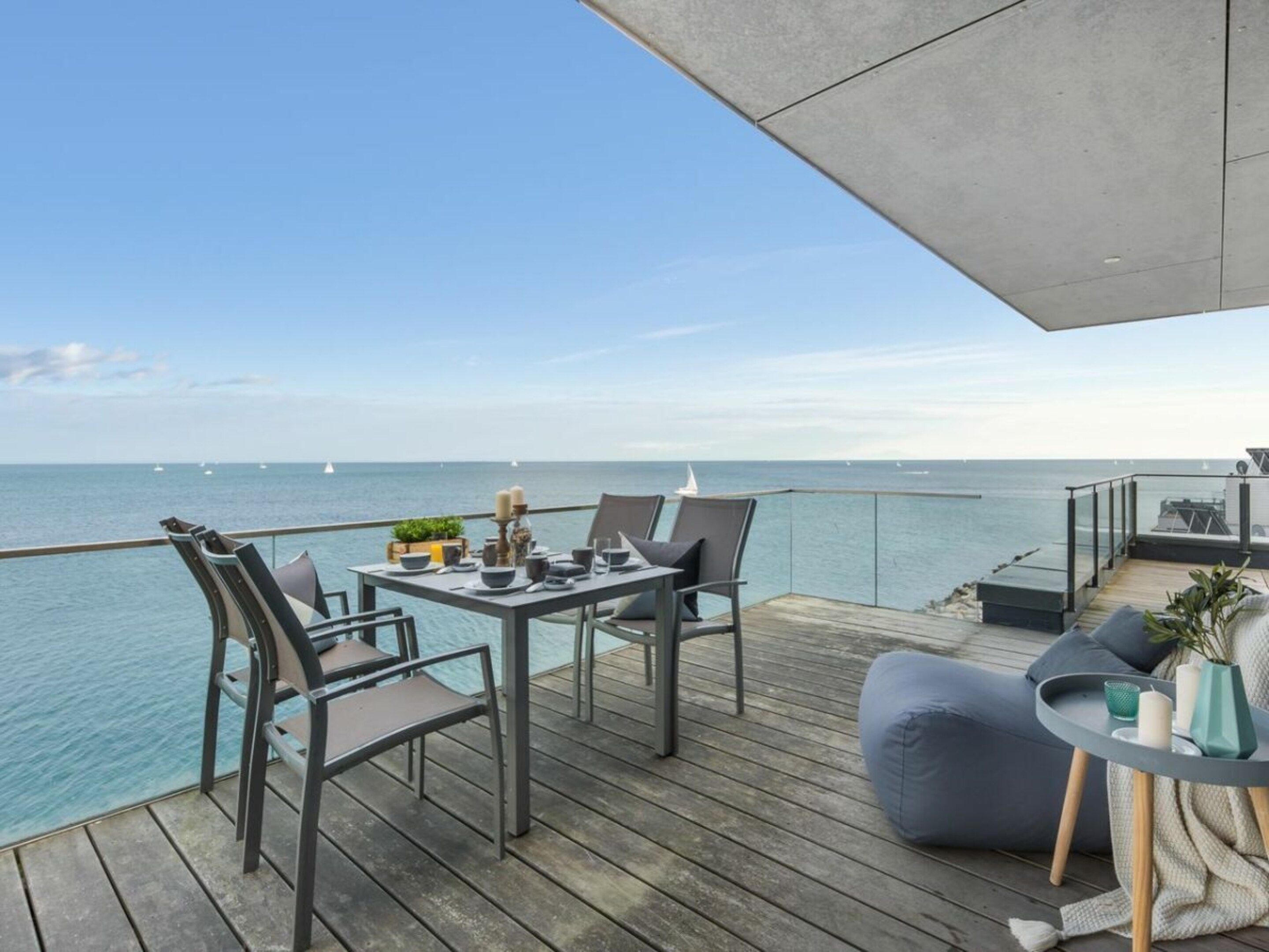 A deck with a table set for two, overlooking the sea with sailboats in the distance.