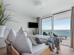 A modern bedroom with a bed, pillows, a TV, and a balcony with a view of the sea. - Penthouse on the Baltic Sea (Kappeln)