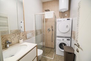 A bathroom with a glass-enclosed shower, a washing machine, and a toilet. - Apartment Gorski Raj (Kranjska Gora)
