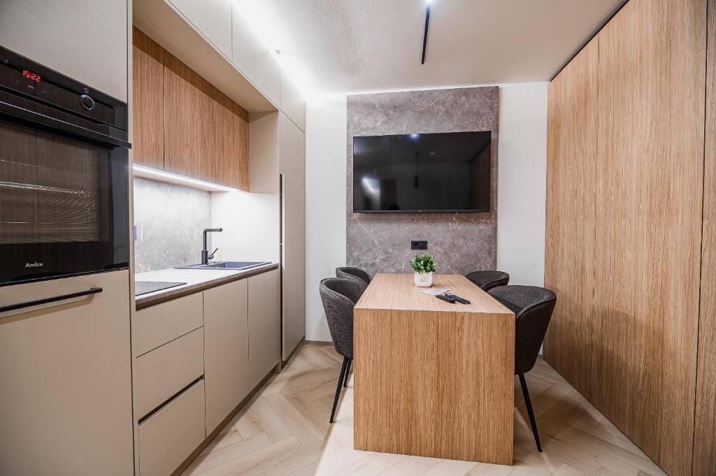 Uma cozinha moderna com forno embutido, área de jantar com mesa e cadeiras de madeira, e uma TV de tela plana fixada na parede.