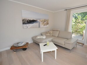 Een moderne woonkamer met een beige bank, een klein wit tafeltje en een houten trolley met tijdschriften.
