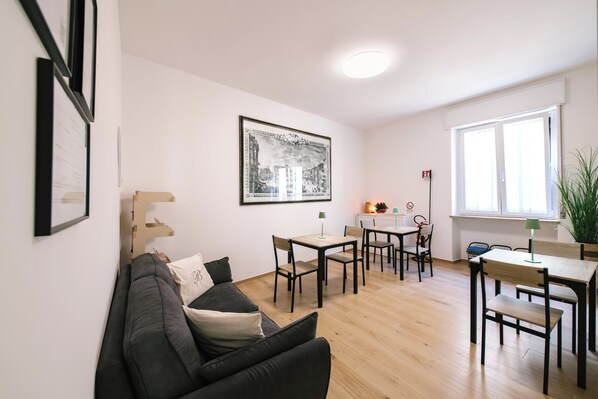 Ein modernes Wohnzimmer mit einer Couch, einem Esstisch mit Stühlen, einem gerahmten Bild an der Wand und einem Fenster mit Blick.