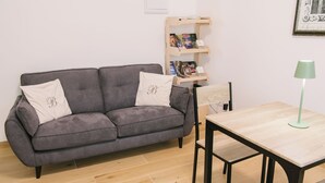 En grå sofa med to puder, et træsidebord, en grøn gulvlampe og en reol med forskellige genstande.
