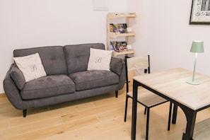 Ein graues Sofa mit zwei Kissen, ein Holztisch, eine grüne Stehlampe und ein Bücherregal mit verschiedenen Gegenständen.