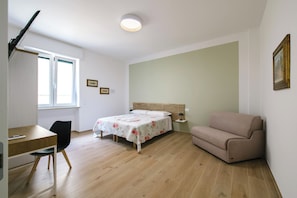 Ein Schlafzimmer mit einem Bett, einem Schreibtisch, einem Stuhl, einem Sofa und einem Fenster.