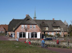 A traditional brick building with a thatched roof and a prominent tower. - Wattengluck at the Little Wood (St. Peter-Ording)