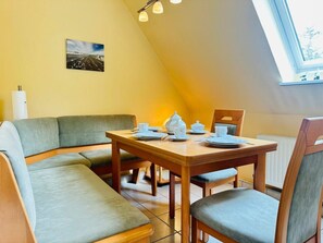 A dining area with a table set for four, a sofa, and a radiator. - Wattengluck at the Little Wood (St. Peter-Ording)