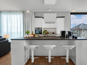 Eine moderne Küche mit Kochinsel, weißen Barhocker, integriertem Backofen und Blick ins Freie.
