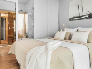 Ein modernes Schlafzimmer mit einem großen Bett, einer Duschkabine aus Glas und einem Gemälde eines Segelboots an der Wand.