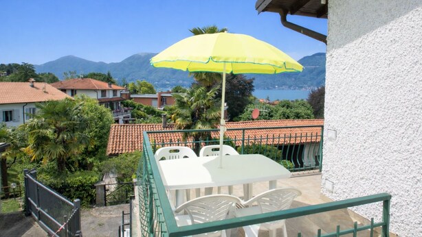 A balcony with a table and chairs, a yellow umbrella, and a view of mountains and water.