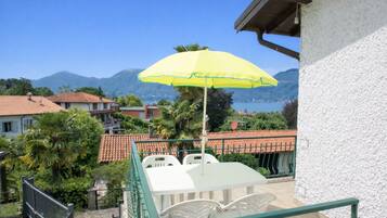 Un balcone con tavolo e sedie, un ombrellone giallo e vista sulle montagne e sull'acqua.