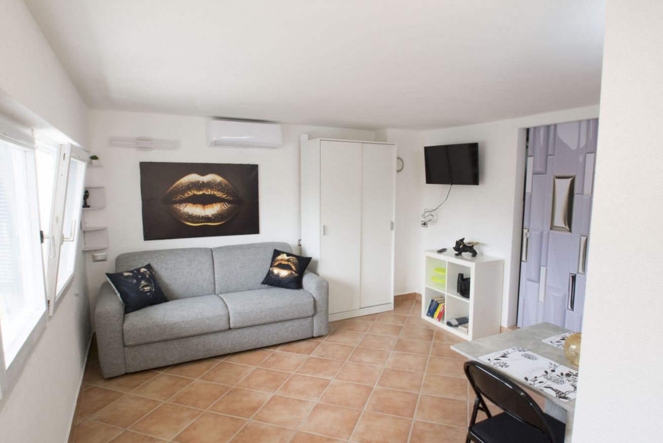 Una sala de estar con un sofá gris, un televisor montado en la pared, una estantería y una puerta.