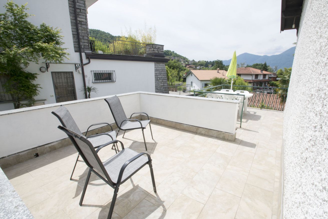 Una terrazza sul tetto con due sedie e un tavolino, affacciata su una zona residenziale con case e montagne sullo sfondo.